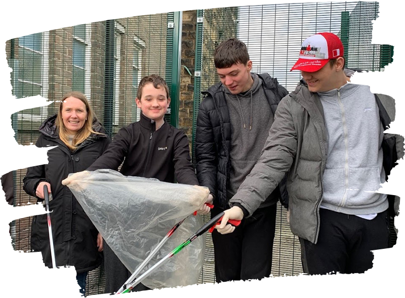 Students and a volunteer with litter pickers and bin bags, stood in front of school gates