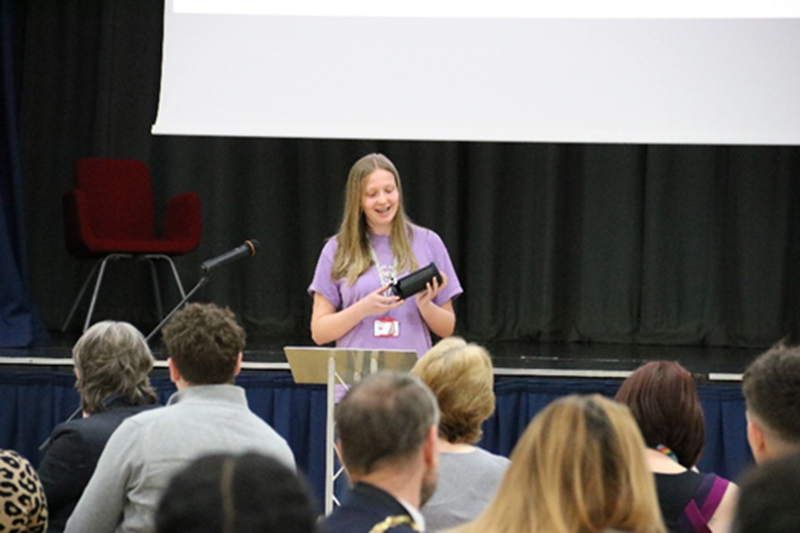 Student standing at a lectern, presenting to an audience