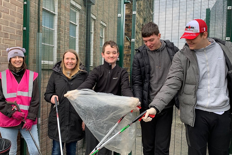 Volunteers and students standing by school gates with litter pickers and bin liners